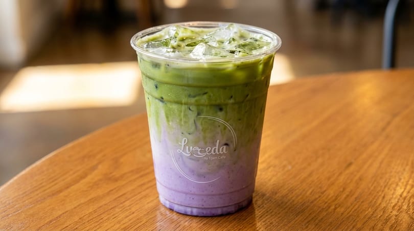 Iced matcha latte with purple taro swirl, topped with ice, on a wooden table.