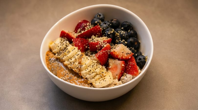A white bowl filled with oatmeal, topped with sliced bananas, strawberries, blueberries, and seeds.